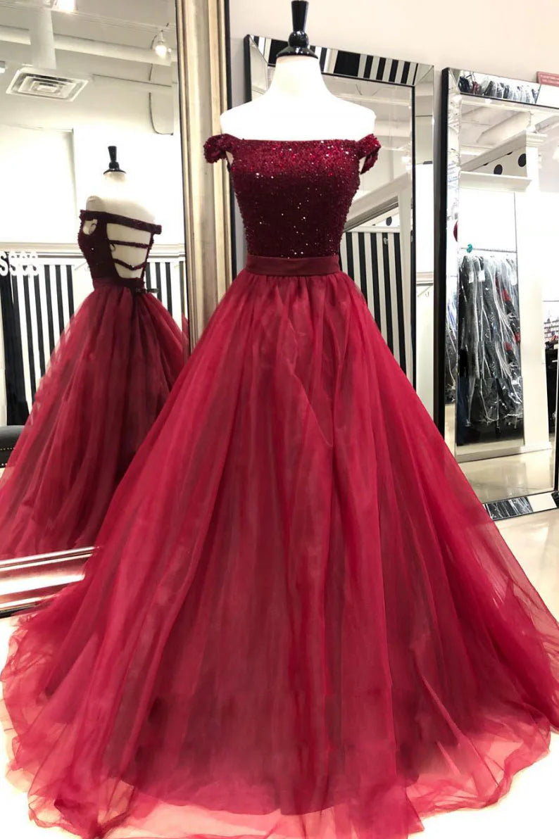Woman in a long burgundy off-shoulder prom dress with sequin and tulle details, posing elegantly.