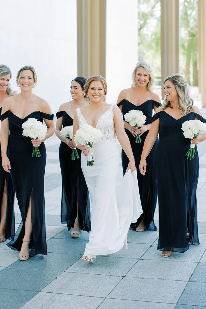 Model wearing a black off-shoulder V-neck long chiffon bridesmaid dress with a side slit.