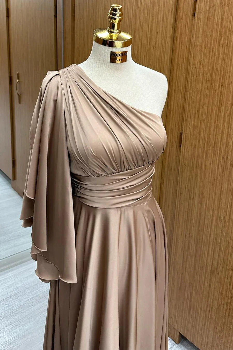 Side view of a woman wearing the champagne one-shoulder formal gown with flared sleeve.