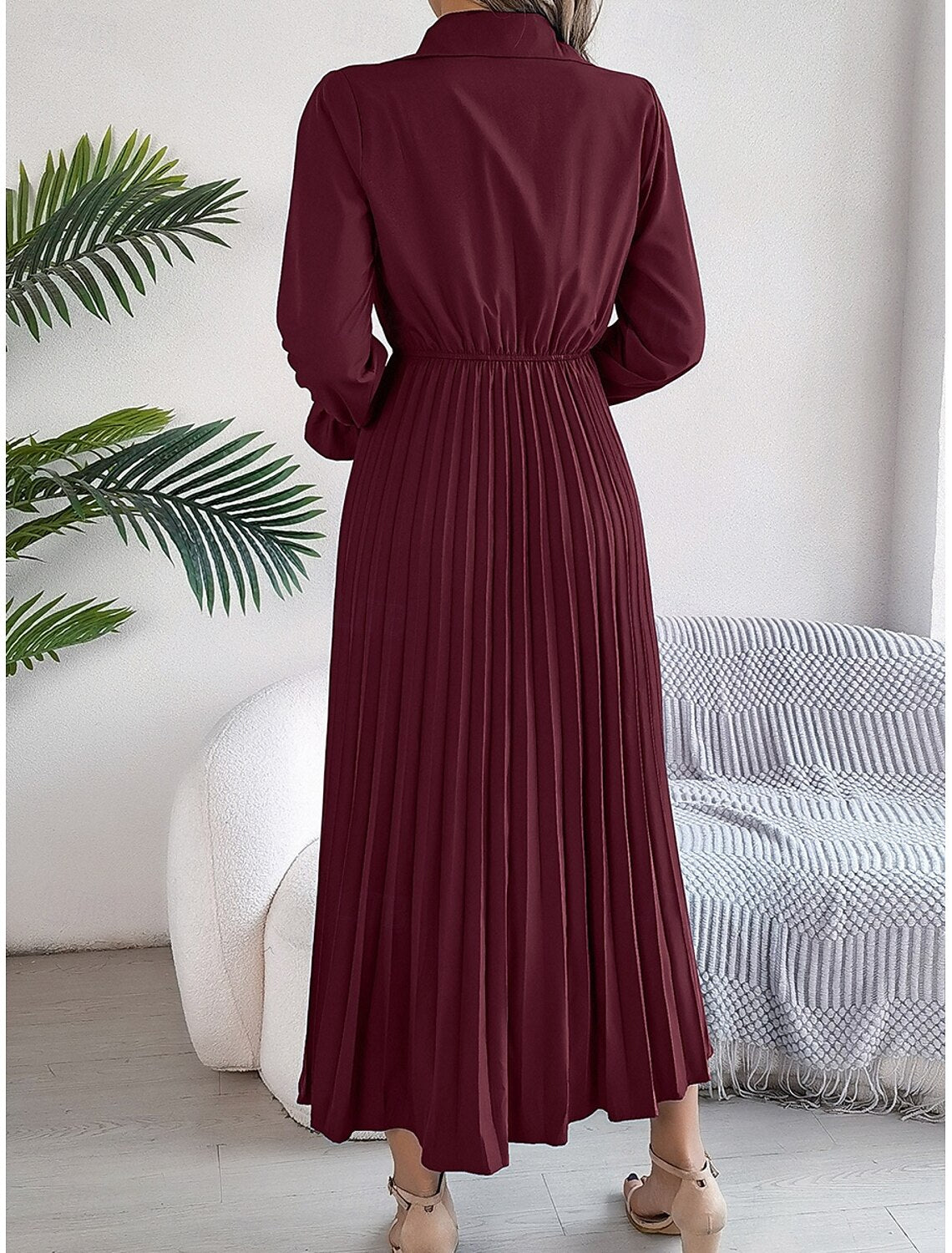 Woman in a plain pleated A-line maxi dress, side view, showcasing the fit and flare silhouette.