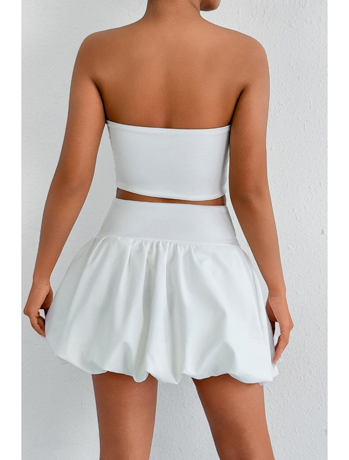 Woman showcasing a white strapless mini dress, back view.