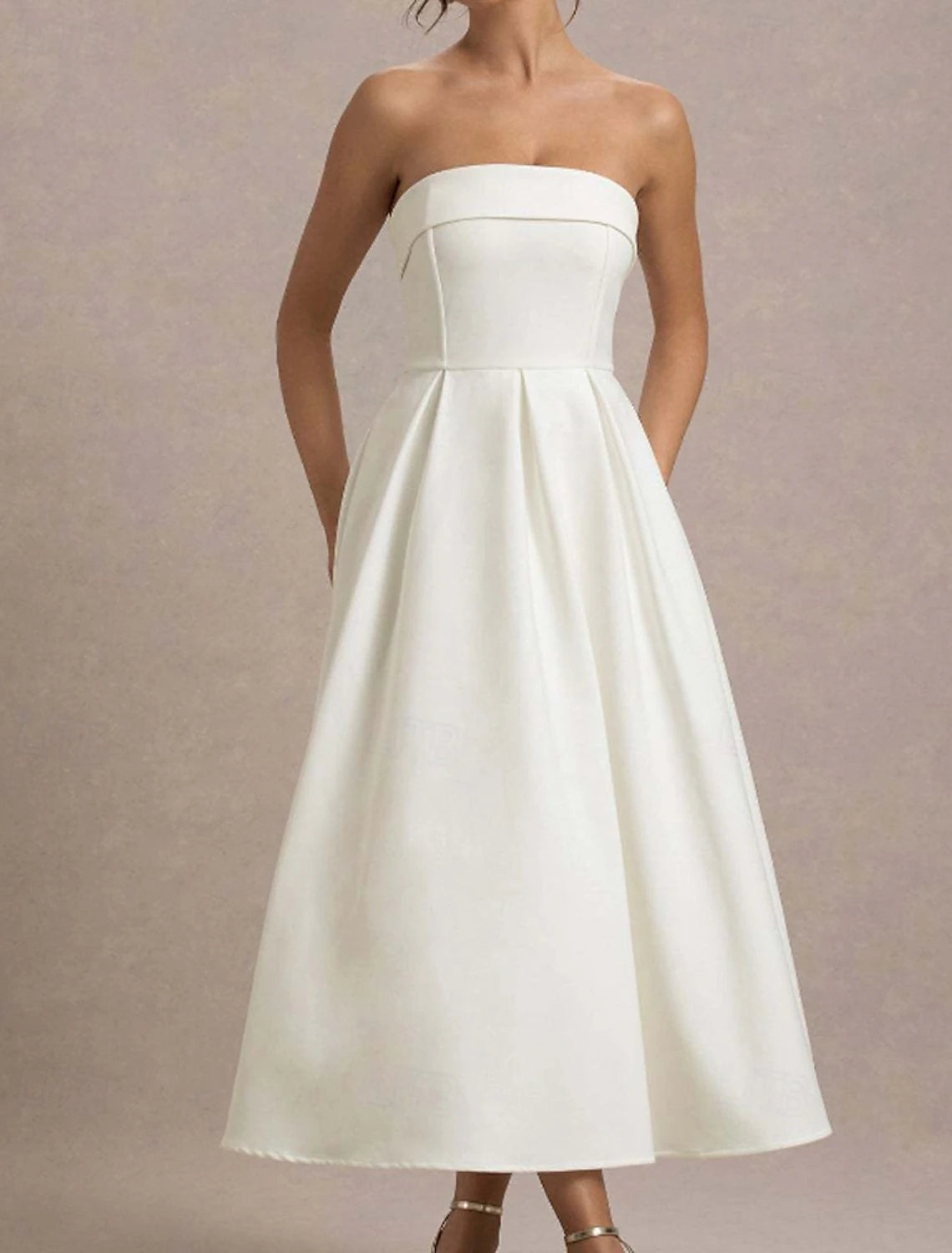 Woman posing in an elegant white strapless midi dress.