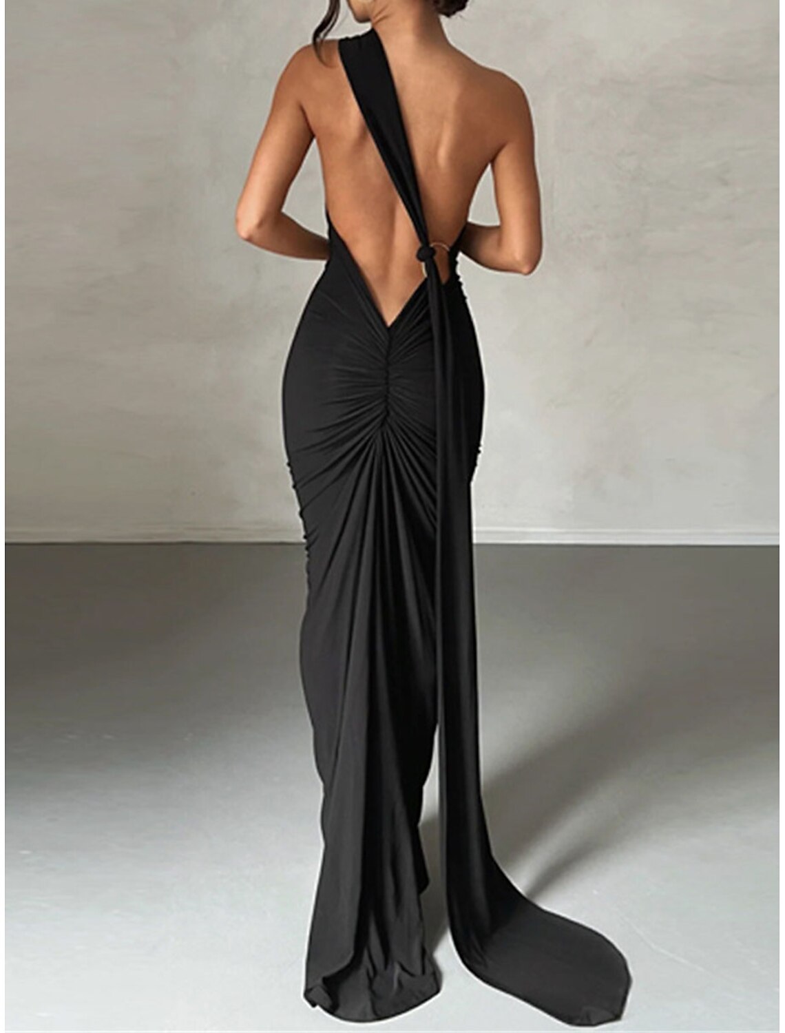 Woman wearing a black ruched backless one-shoulder special occasion dress.