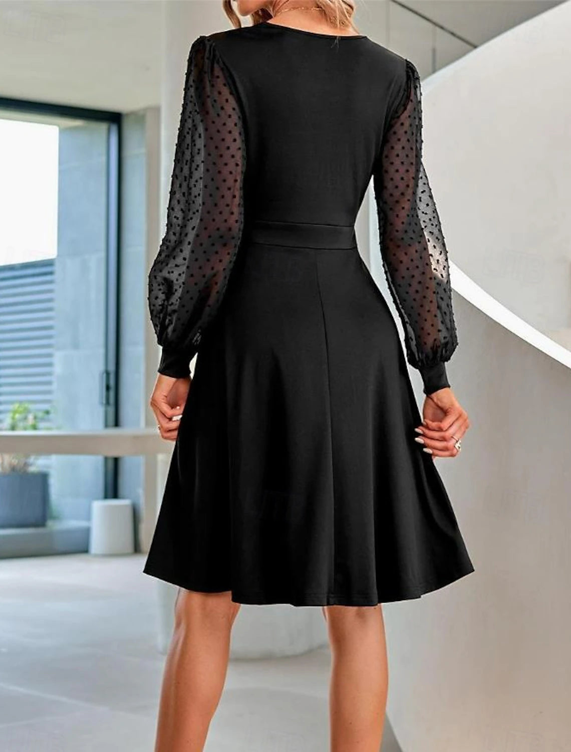Back view of a woman in a black ruched mesh mini dress with bishop sleeves.