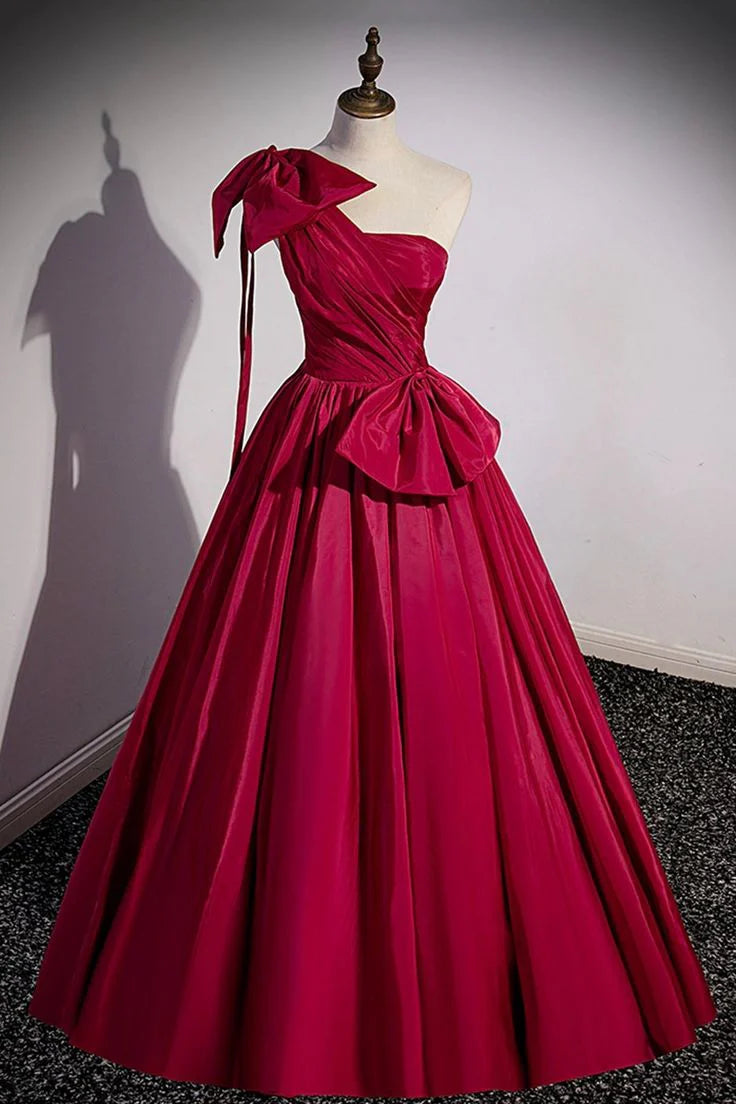 Woman in an elegant one-shoulder long satin evening dress with a prominent bow detail.
