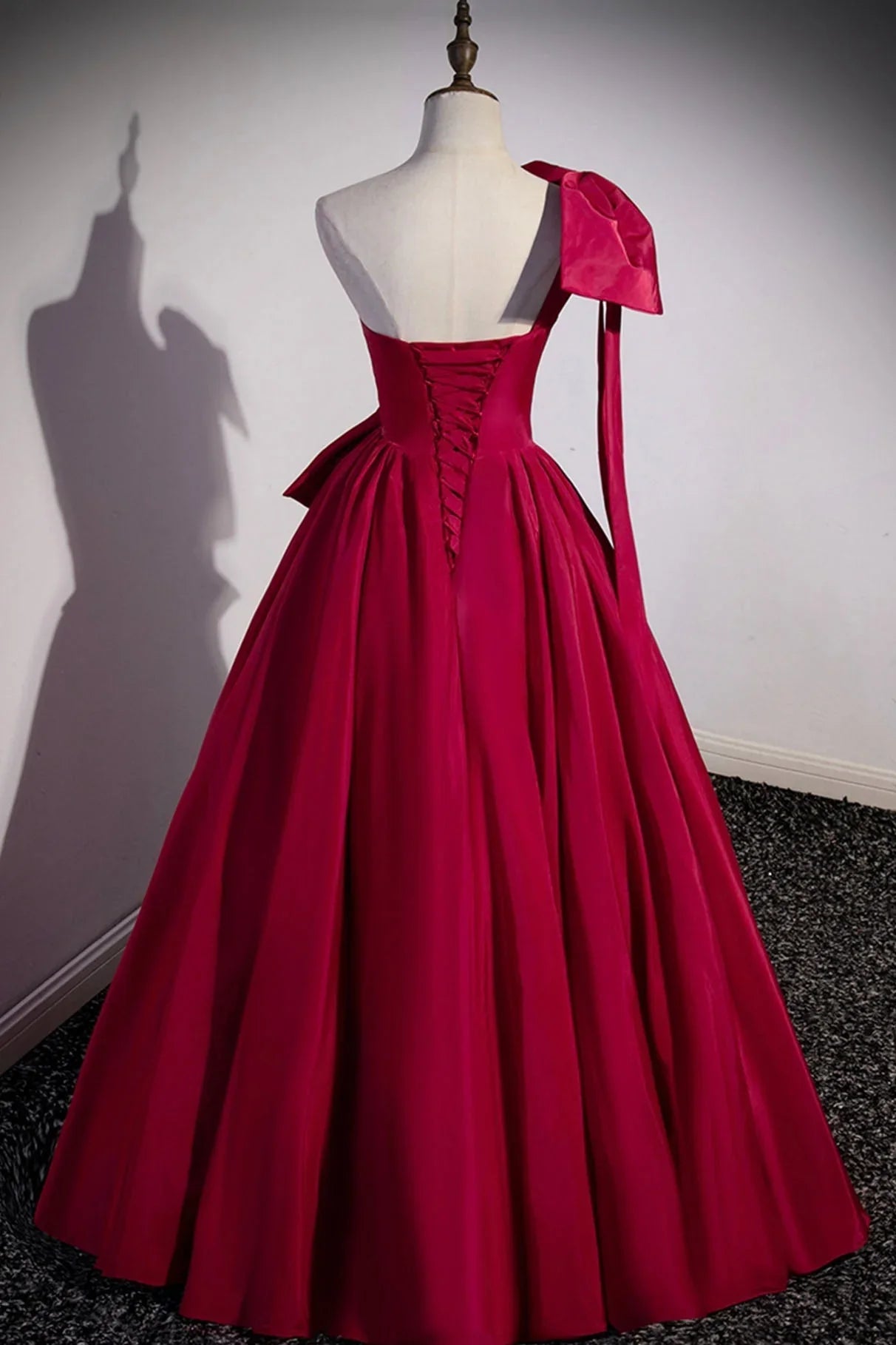 Back view of a woman wearing a long satin evening dress, showcasing the one-shoulder design and bow.