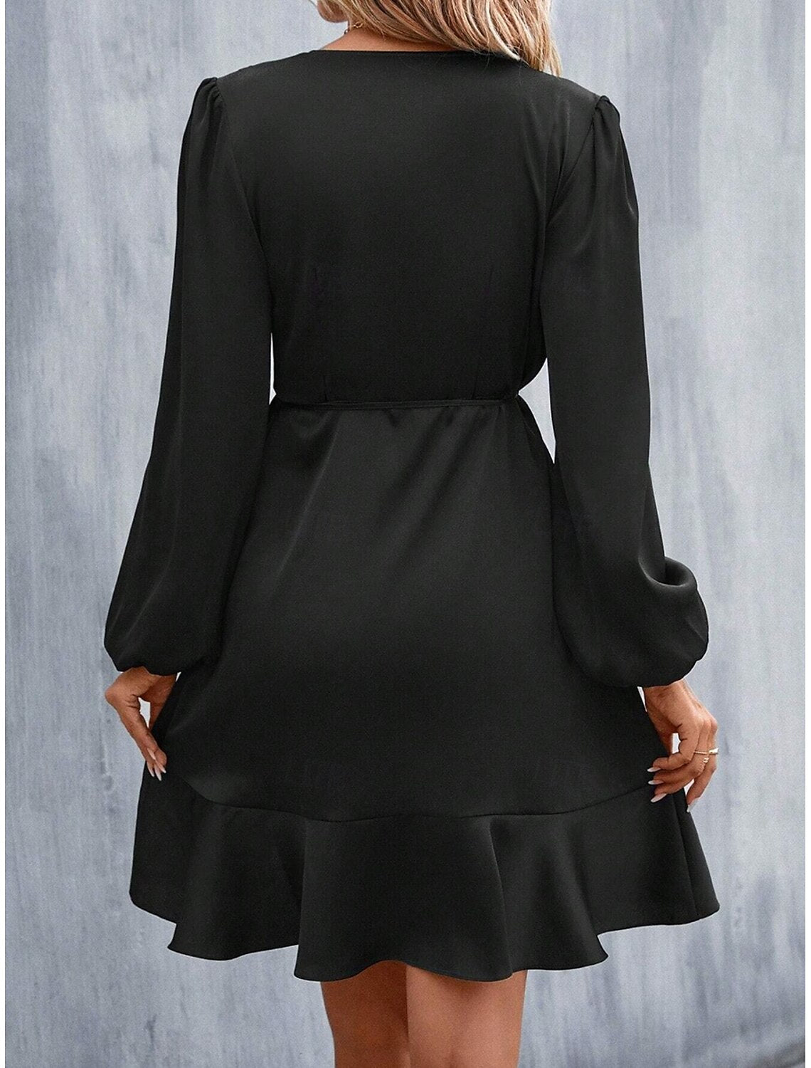 Woman wearing a black ruffle patchwork mini dress with V-neck and long sleeves, side view.
