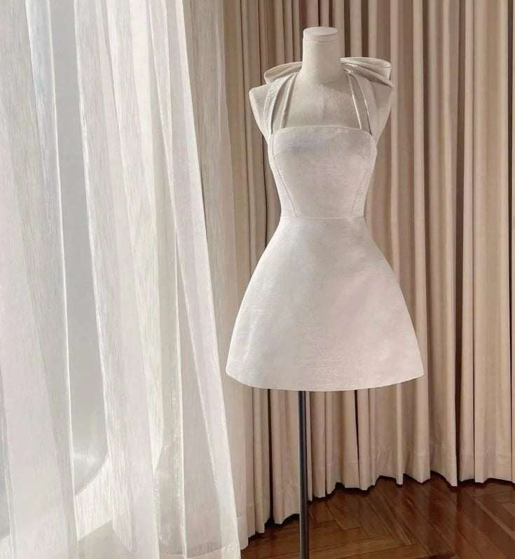 Model wearing an elegant light pink satin A-line mini homecoming dress with square neck and halter straps.