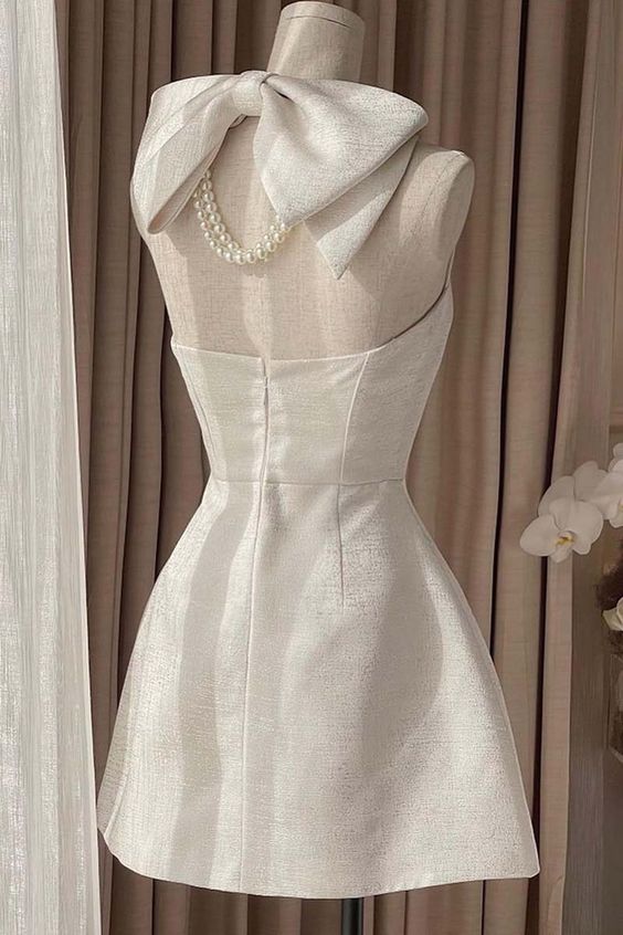 Back view of a light pink satin mini dress, highlighting the halter neckline and a decorative bow.