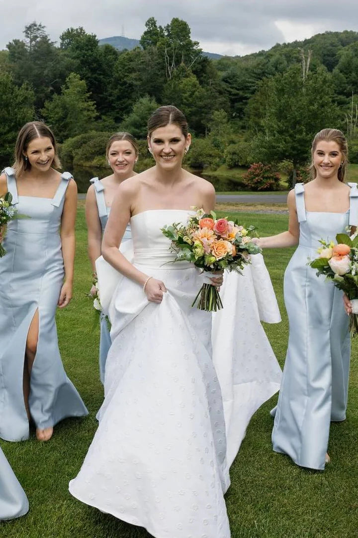 Elegant satin long bridesmaid dress with delicate straps, bow detail, pleats, and a high slit, worn by a model.