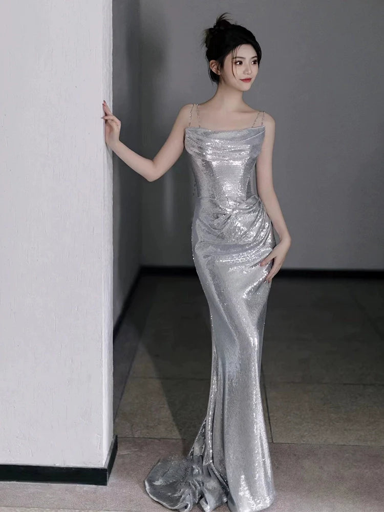 Model wearing a silver sequin mermaid evening dress with spaghetti straps, front view.