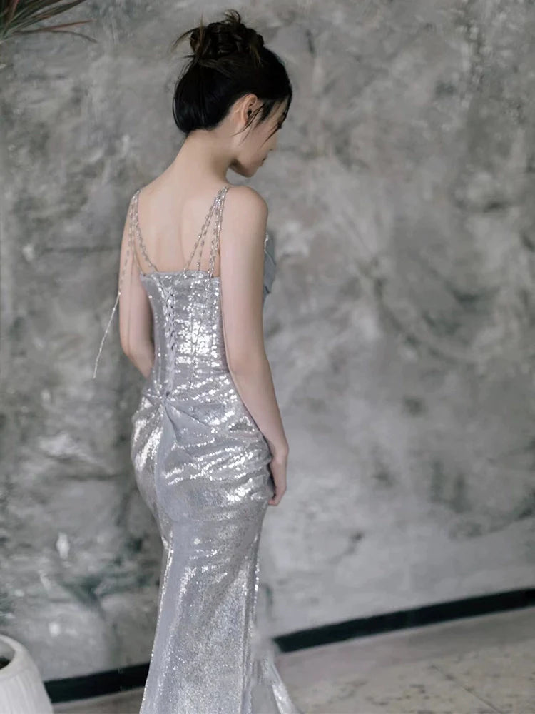 Back view of a model wearing a silver sequin mermaid evening dress with spaghetti straps.