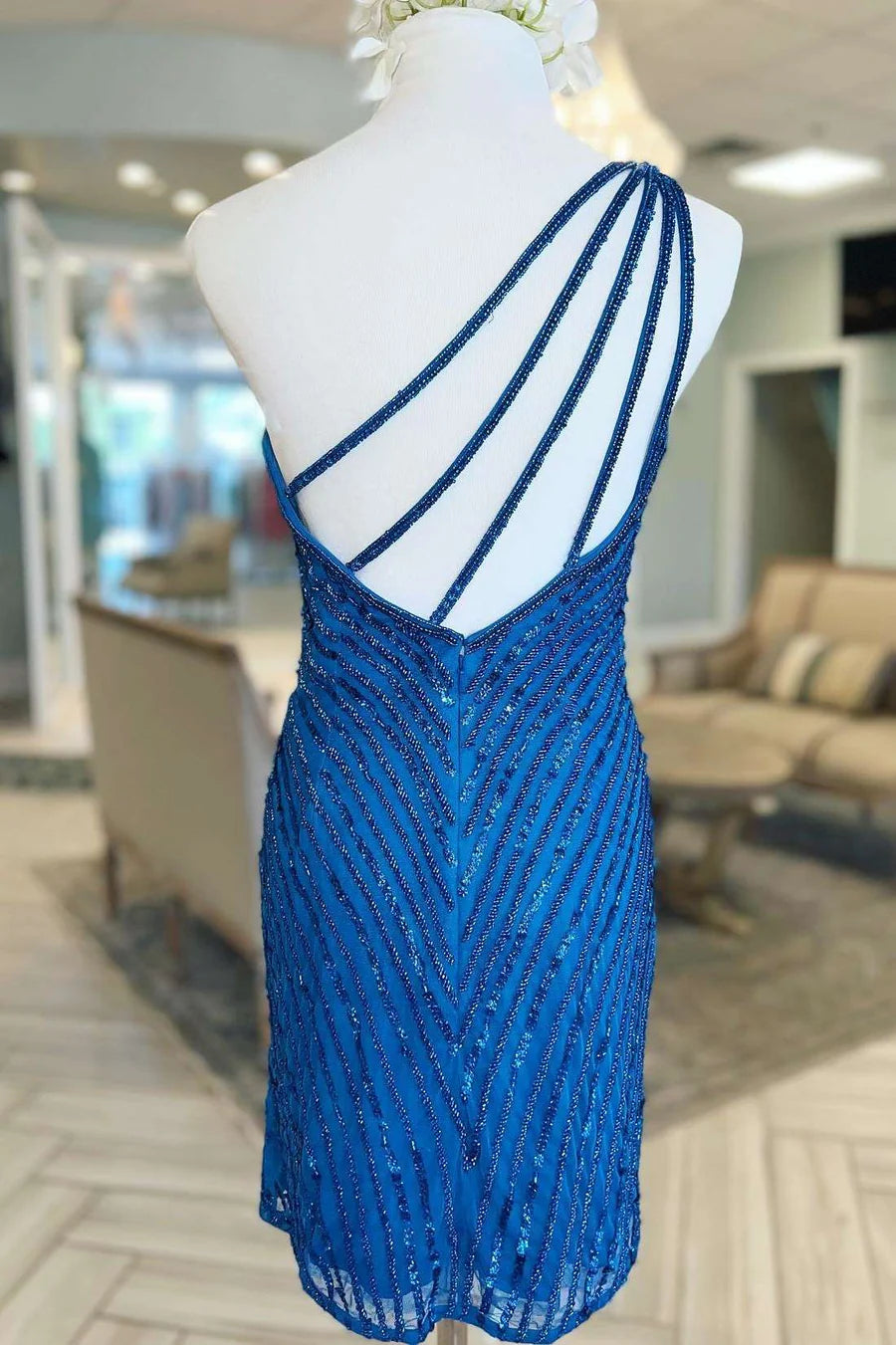 Side view of a woman in a blue one-shoulder beaded mini cocktail dress, showcasing the slim fit.