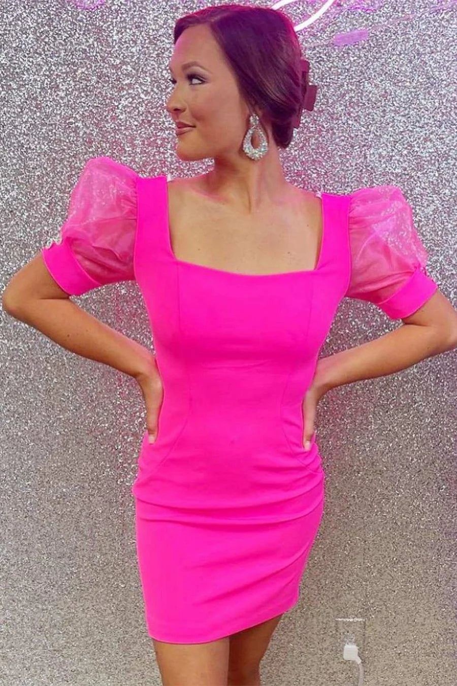 Woman in a neon pink square neck bodycon party dress with sheer sleeves, side view.