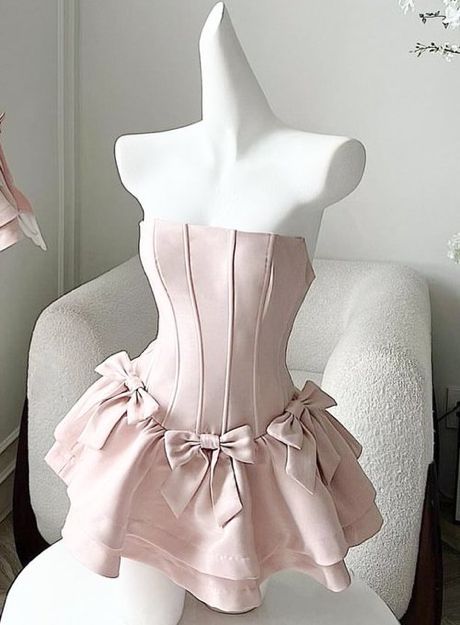 Model wearing a light pink strapless corset short homecoming dress with bow details and a ruffled skirt.