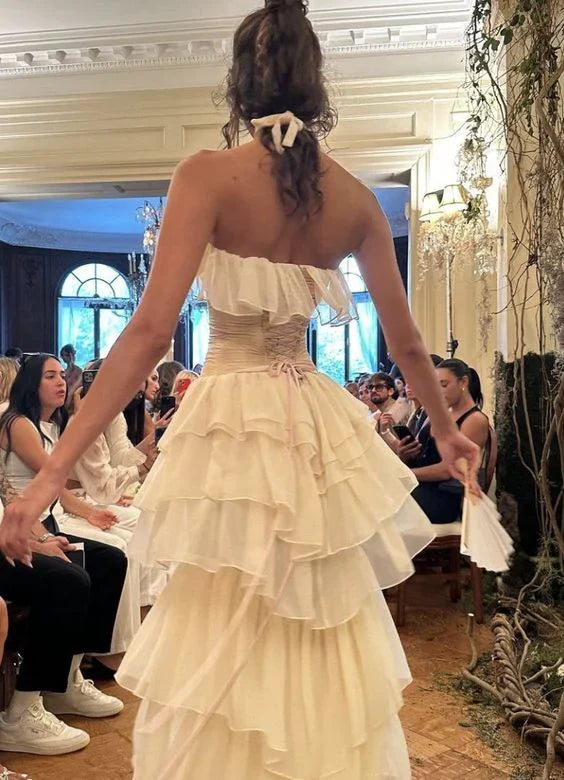 Model showcasing the back of an ivory strapless tiered chiffon gown.