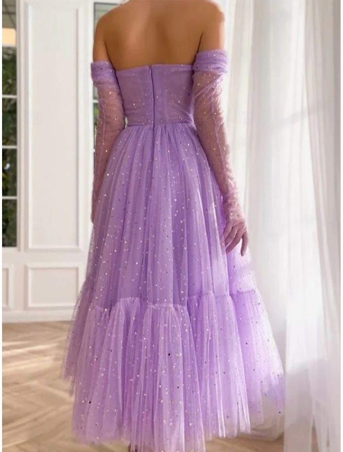 Woman wearing an elegant purple off-shoulder tulle maxi dress, side view.
