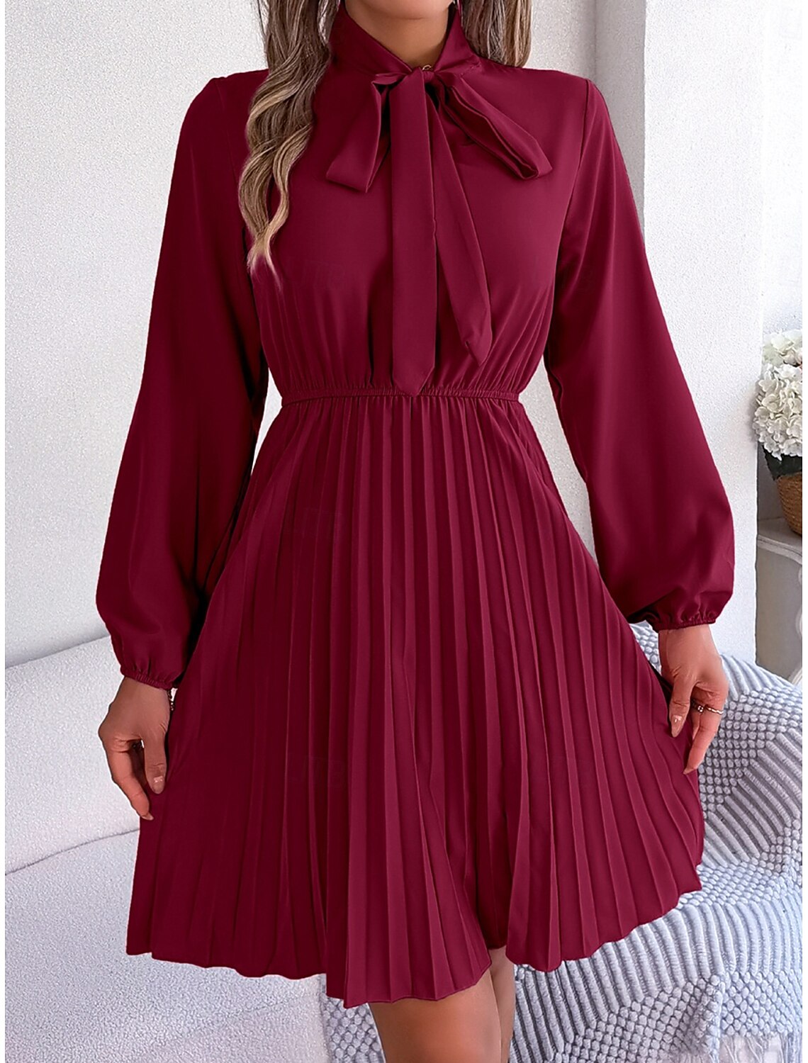 Woman wearing an elegant V-neck long sleeve pleated mini wrap dress.
