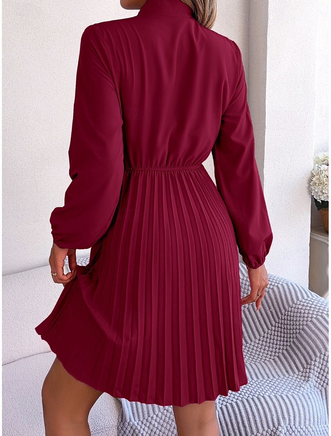 Woman posing in a solid color A-line mini dress with pleated detail.