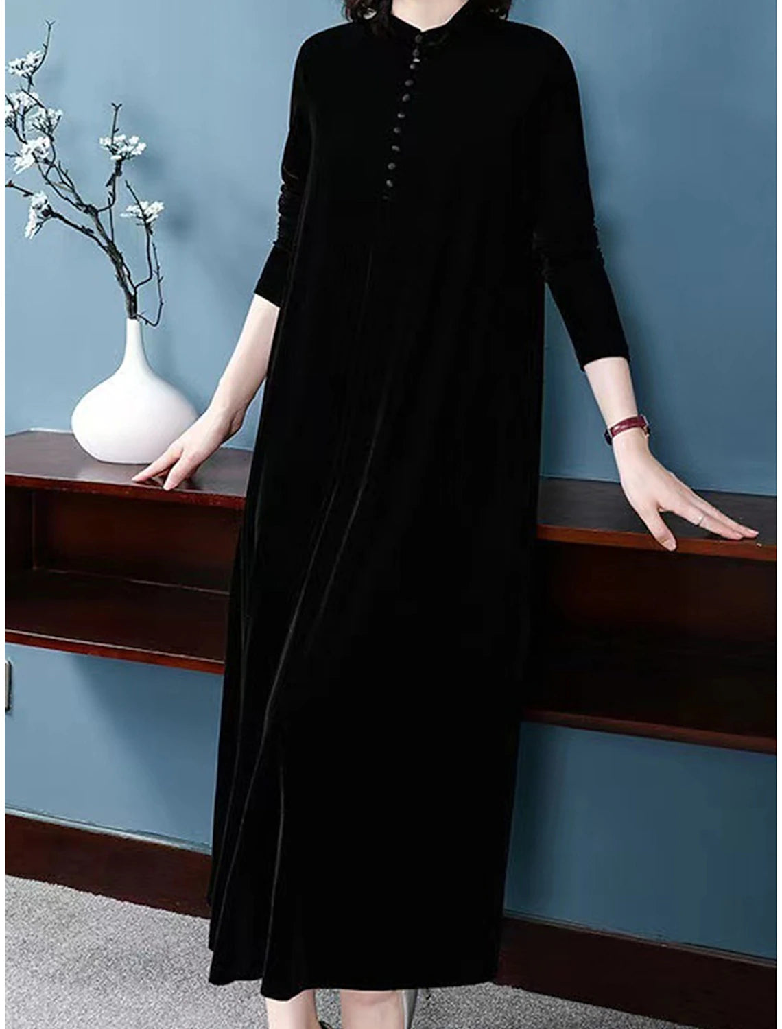 Woman wearing an elegant black velvet long sleeve dress with button details, posing gracefully.