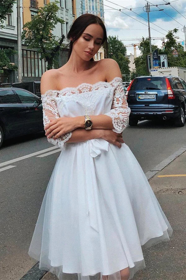 Woman wearing a white off-the-shoulder knee-length tulle homecoming dress with lace details.