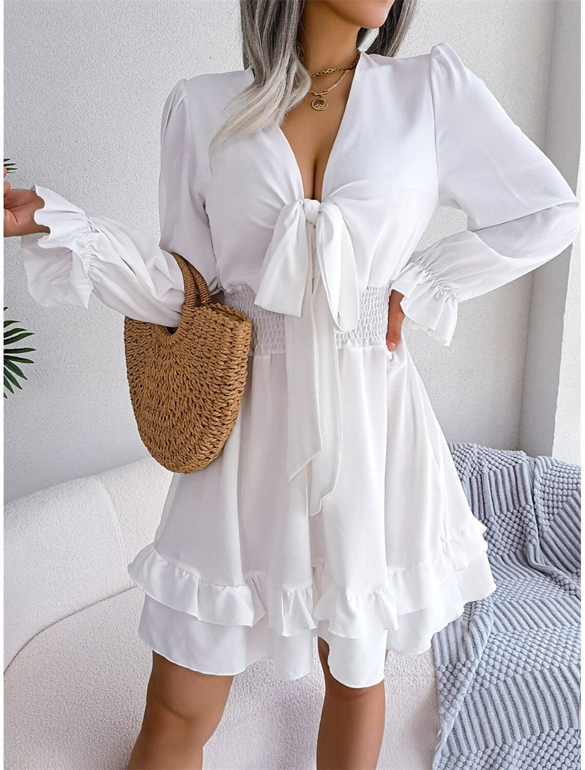 Side view of a woman in a stylish white V-neck long sleeve A-line mini dress.