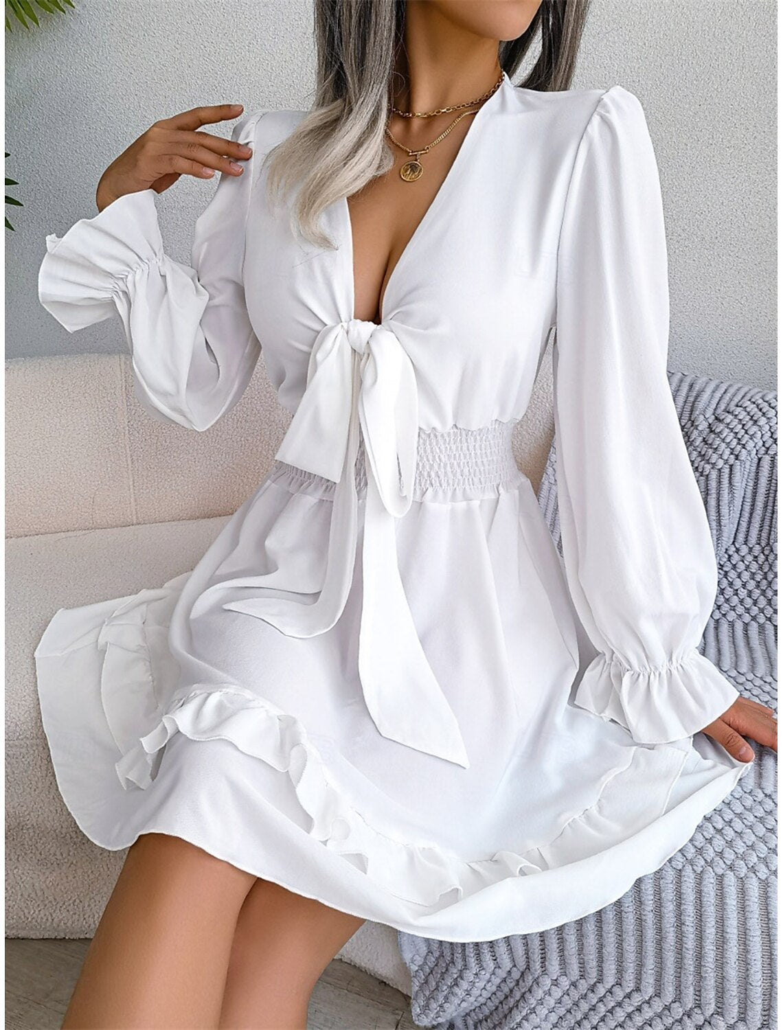 Back view of a woman in a chic white V-neck long sleeve A-line mini dress.