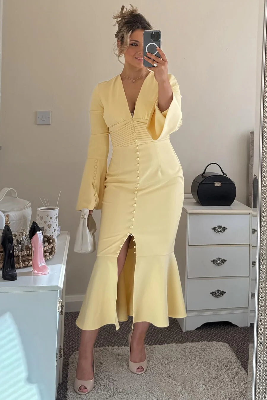 Model posing in a glamorous yellow V-neck mermaid wedding guest dress with bell sleeves.