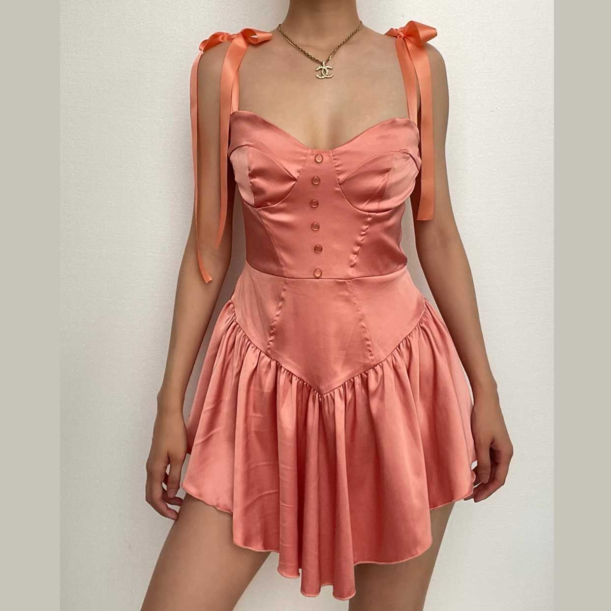 Model wearing a peach pink A-line sweetheart mini homecoming dress with tie-shoulder straps and ruffled hem.