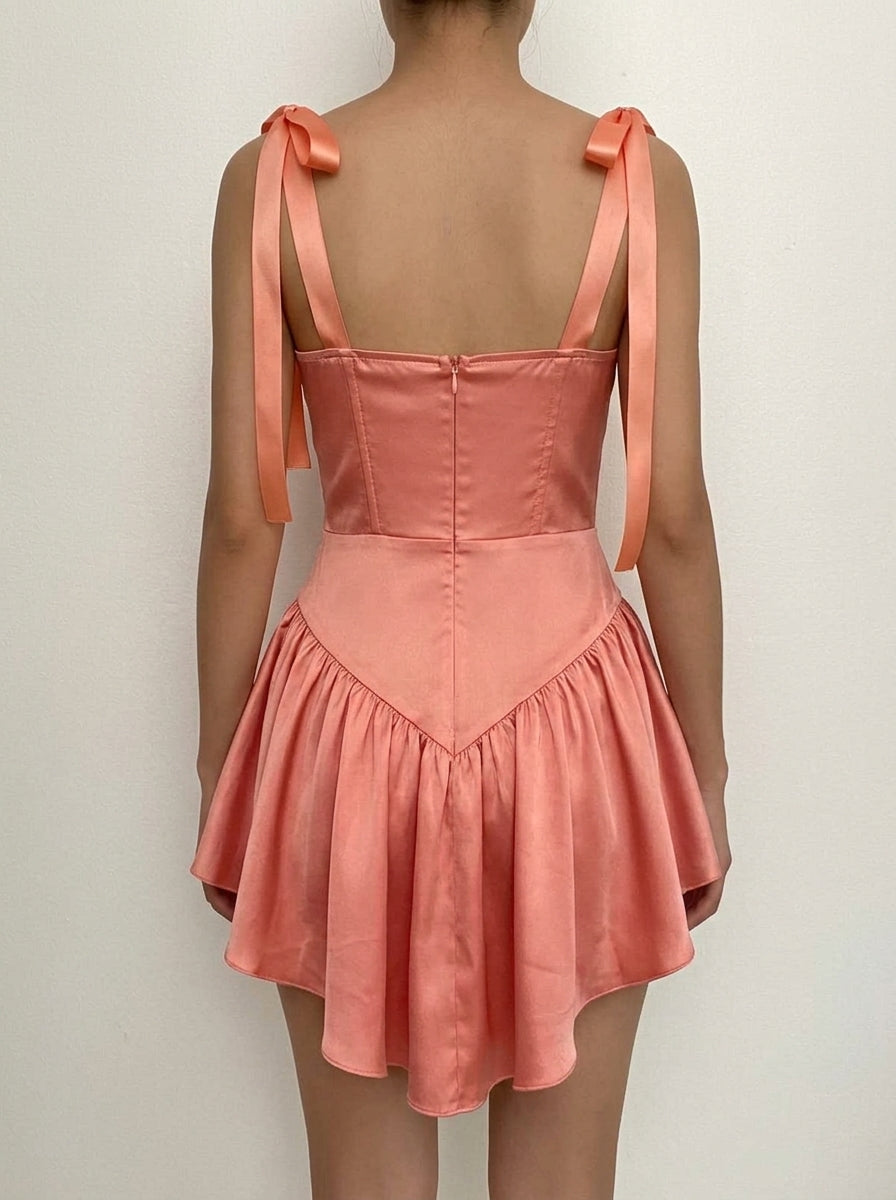 Side view of a model in a peach pink A-line mini dress, showcasing the tie-shoulder straps and ruffled hem.