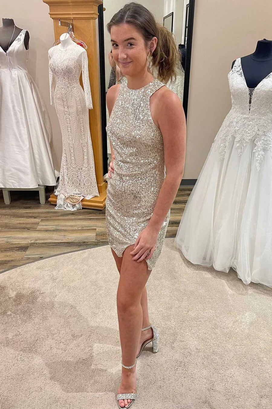 Woman wearing a silver sequin fitted halter dress with an open back and side slit.