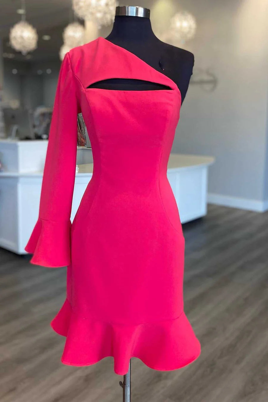 Woman wearing a neon pink one-sleeve, one-shoulder mermaid cocktail gown with keyhole detail.
