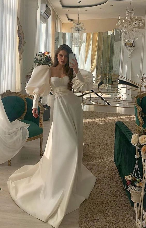 Woman wearing an ivory long sleeve satin A-line evening gown.