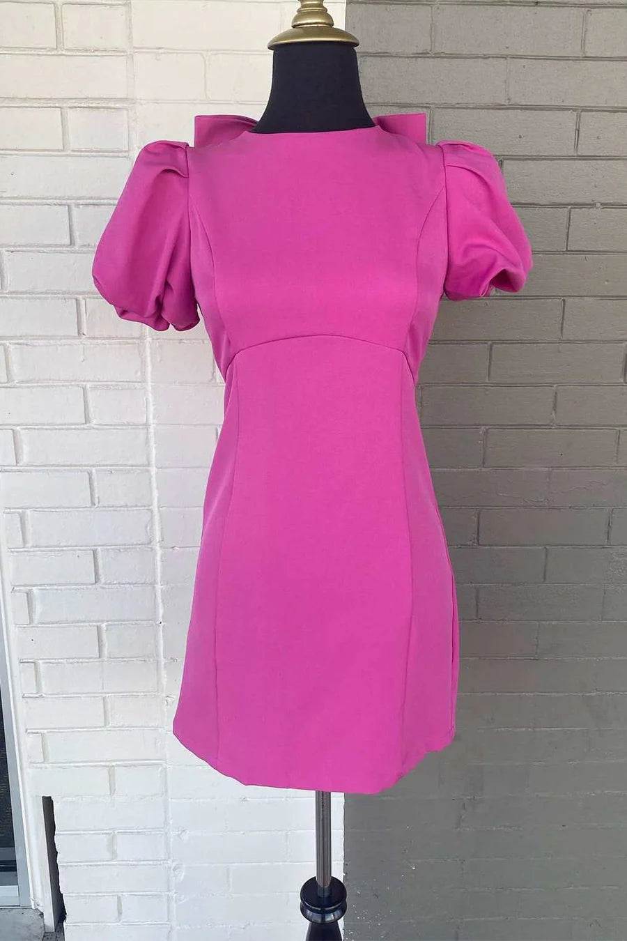 Front view of a woman wearing a neon pink short homecoming dress with puff sleeves and a crew neck.