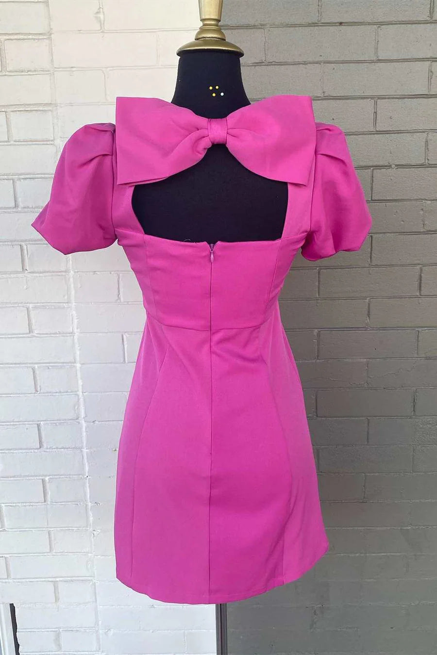 Back view of a woman in a neon pink short homecoming dress, highlighting the bow detail.