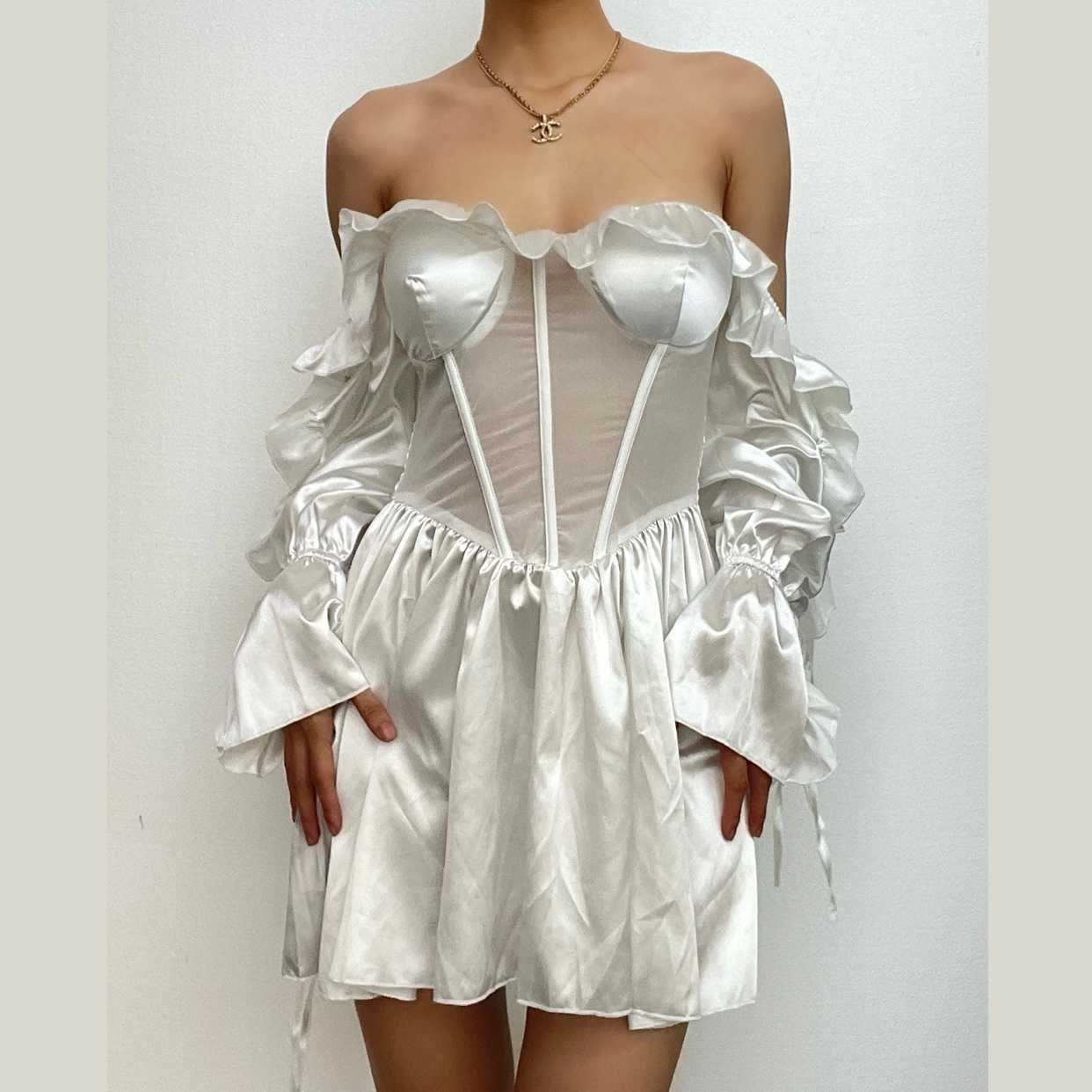 Model wearing a white A-line off-shoulder mini homecoming dress with ruffled long sleeves and a corset bodice.