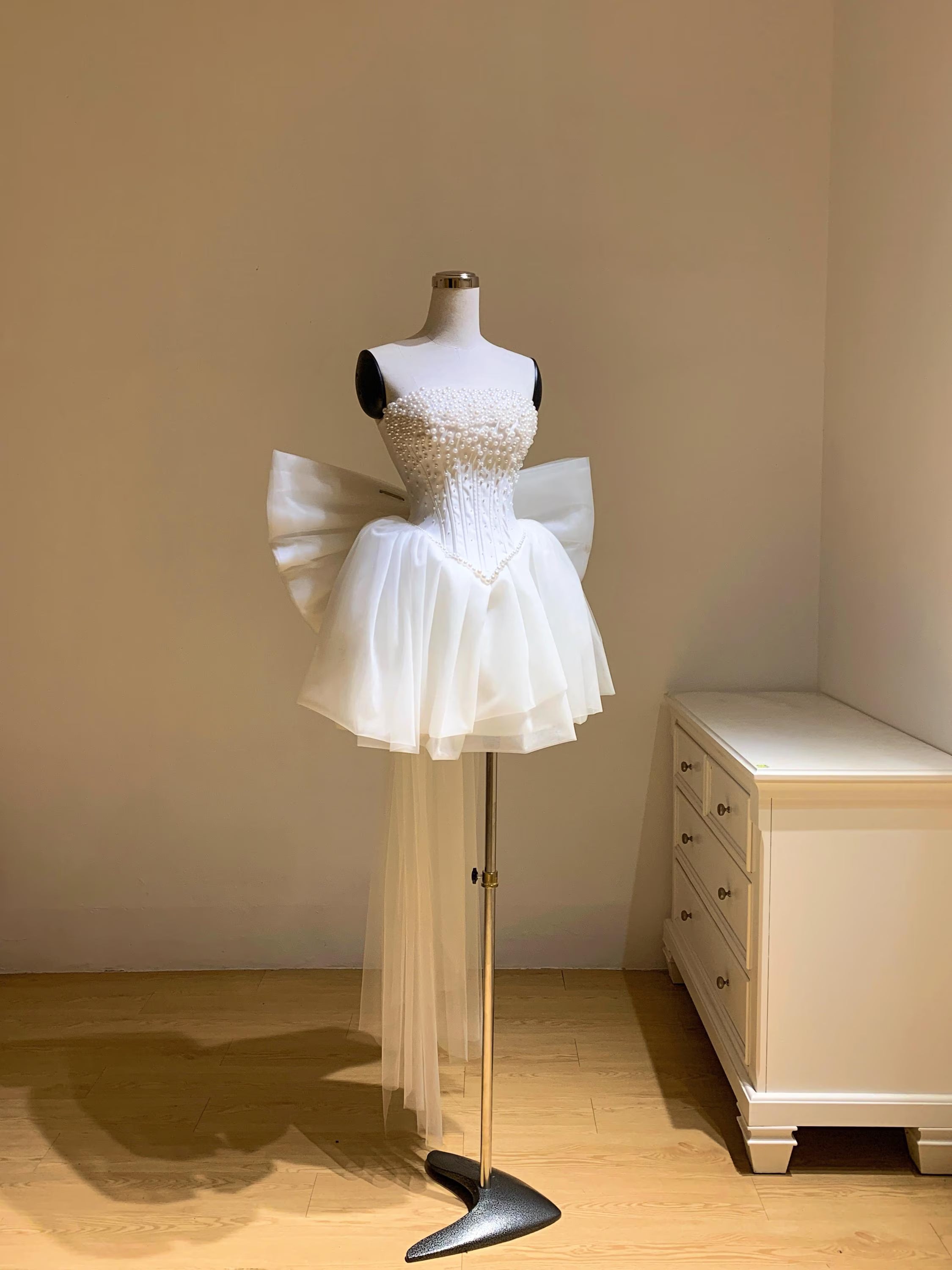 Woman wearing a white strapless A-line mini homecoming dress with pearl corset and large back bow.