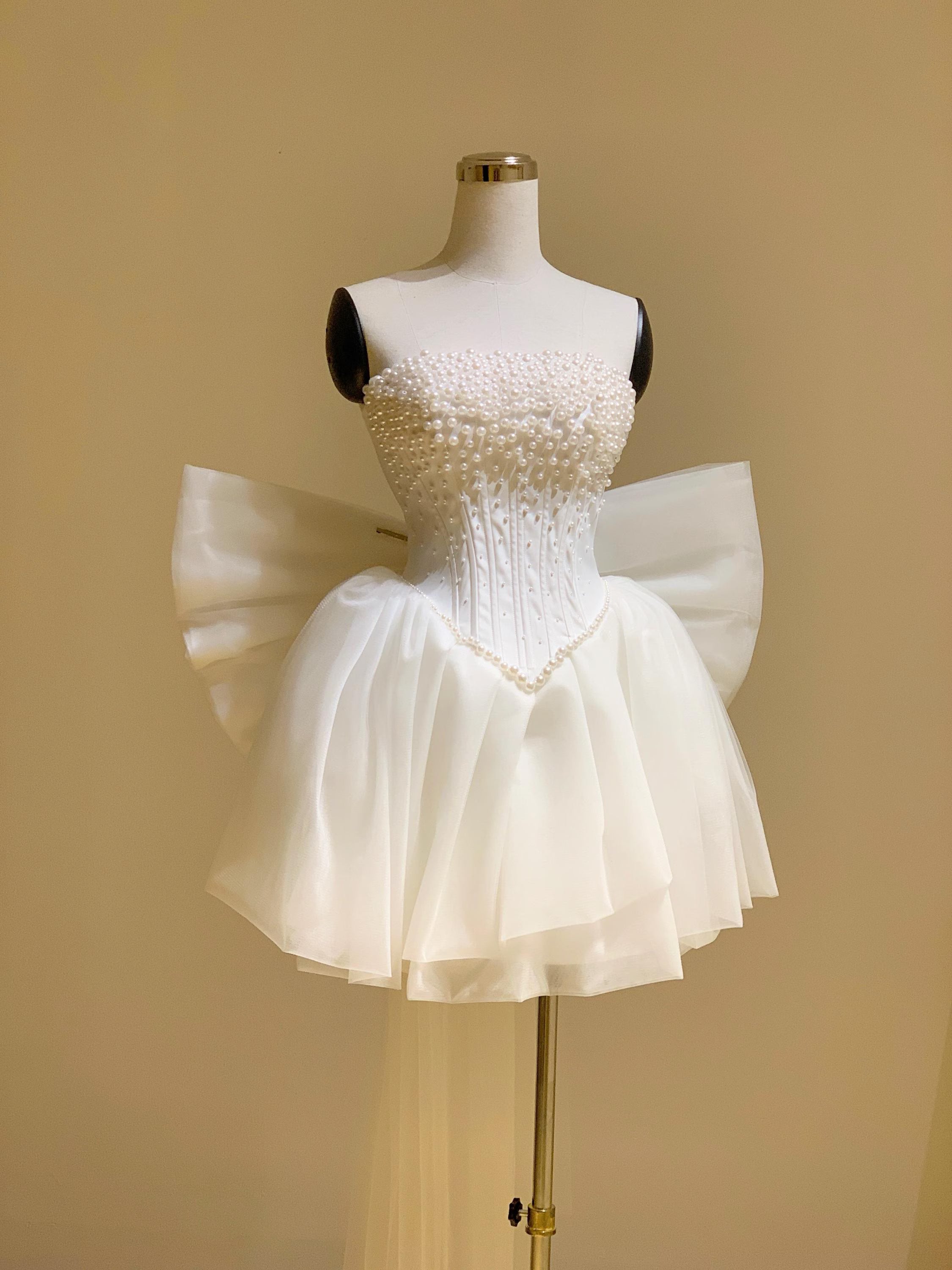 Back view of the white A-line mini dress, showing the oversized bow and sheer train.