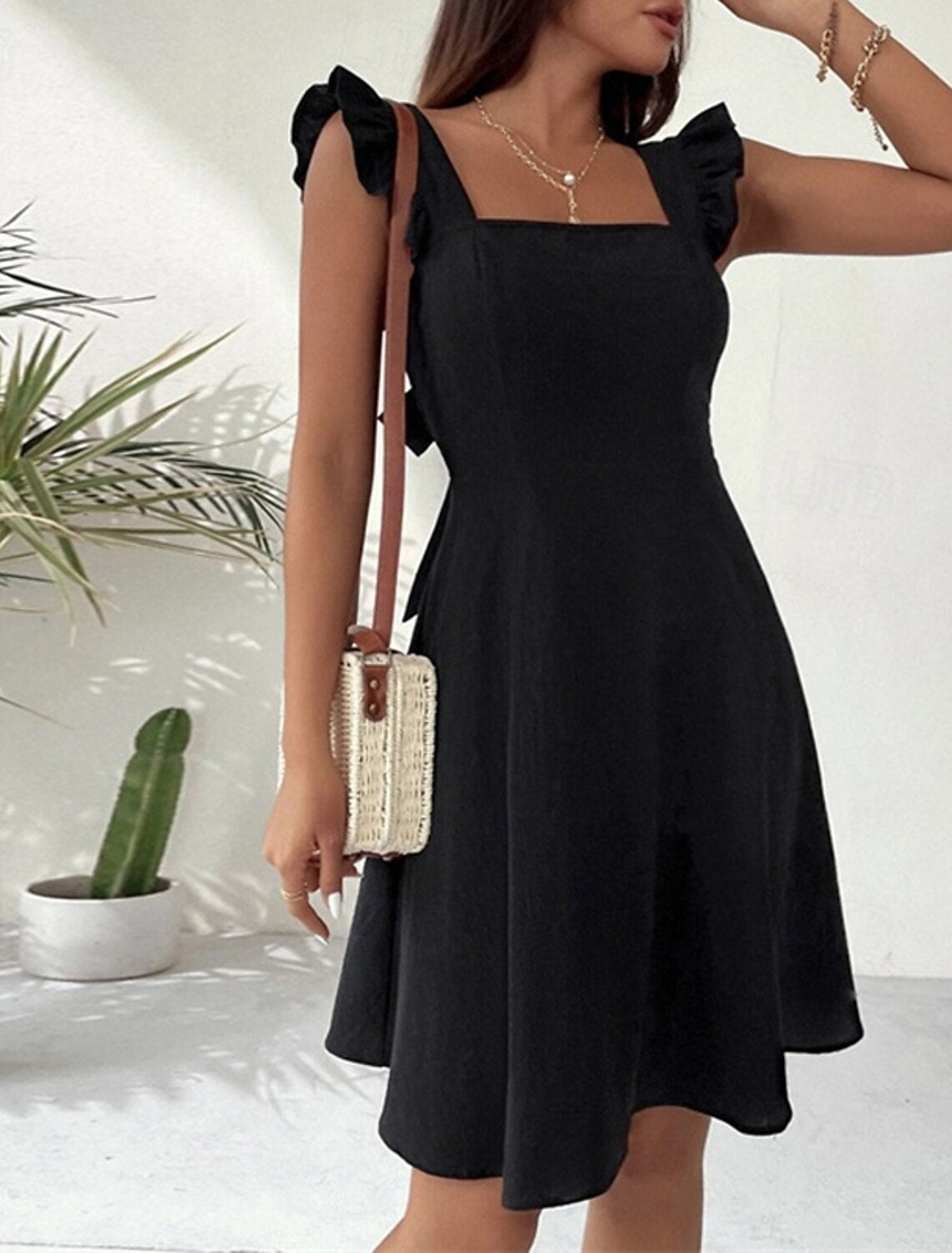 Woman posing in a fashionable solid mini dress with square neck and butterfly sleeves.